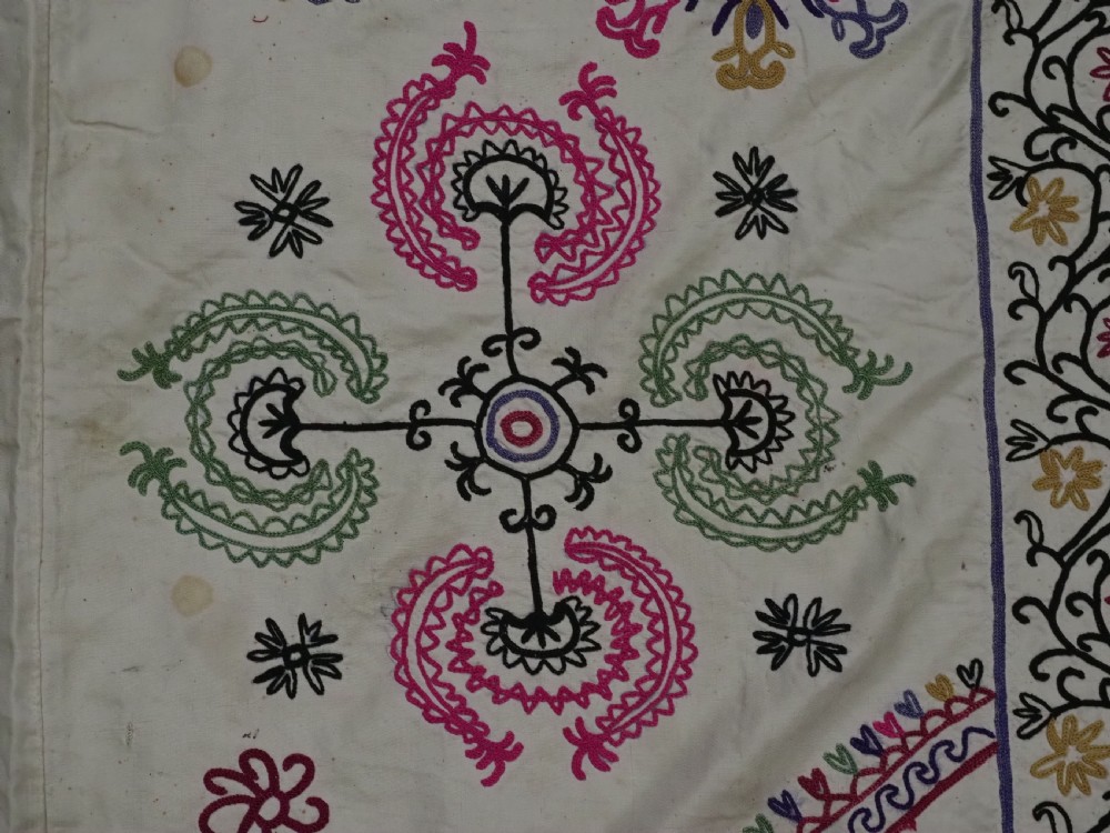 A rectangular antique cream silk Suzani textile featuring hand embroidery with multi-coloured floral roundels and vine borders. View VI