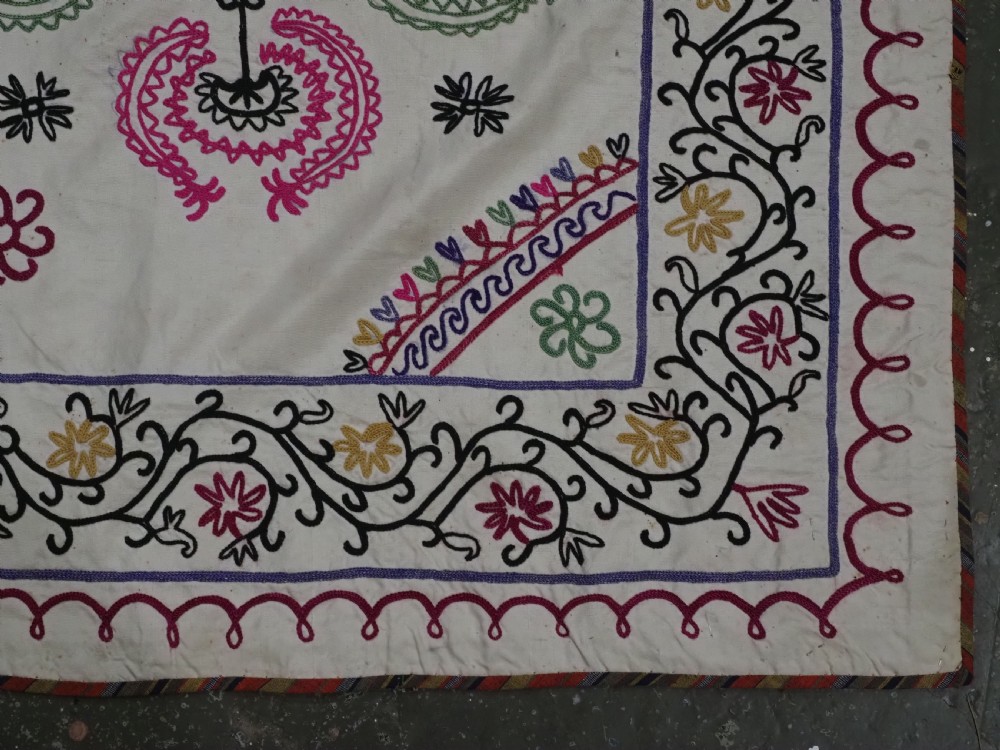A rectangular antique cream silk Suzani textile featuring hand embroidery with multi-coloured floral roundels and vine borders. View VII