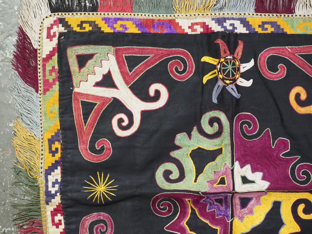 A square black textile panel featuring multicoloured silk embroidery with scroll and geometric motifs bordered by a fringe edge. View II