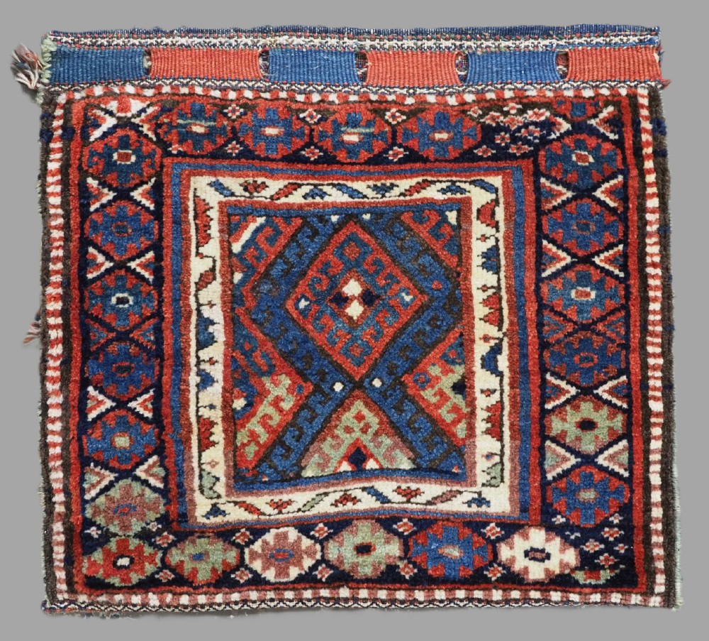 A hand-woven antique Kurdish Jaf bag featuring geometric diamond latch-hook motifs in red, blue, and cream wool with woven loops along the top edge.