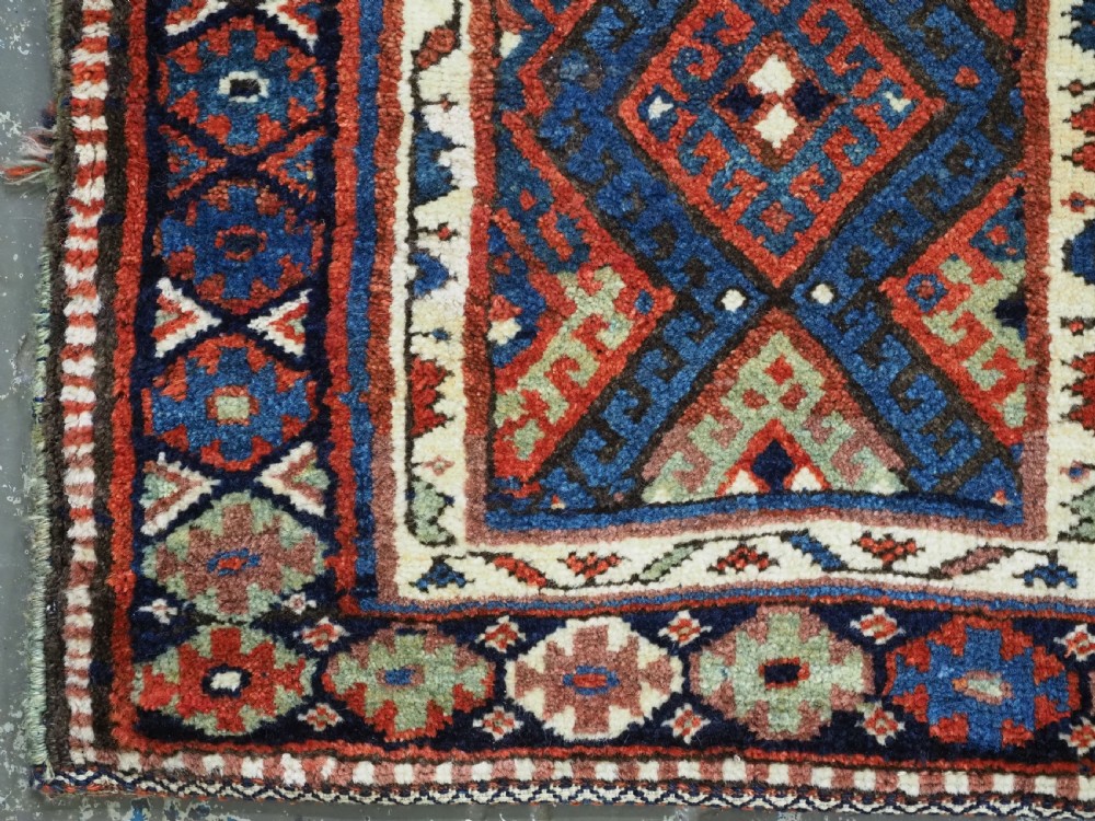 A hand-woven antique Kurdish Jaf bag featuring geometric diamond latch-hook motifs in red, blue, and cream wool with woven loops along the top edge. View IV