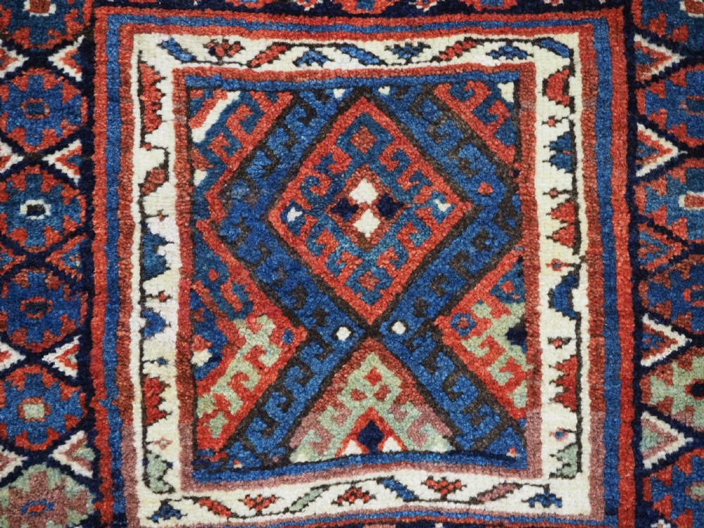 A hand-woven antique Kurdish Jaf bag featuring geometric diamond latch-hook motifs in red, blue, and cream wool with woven loops along the top edge. View VII