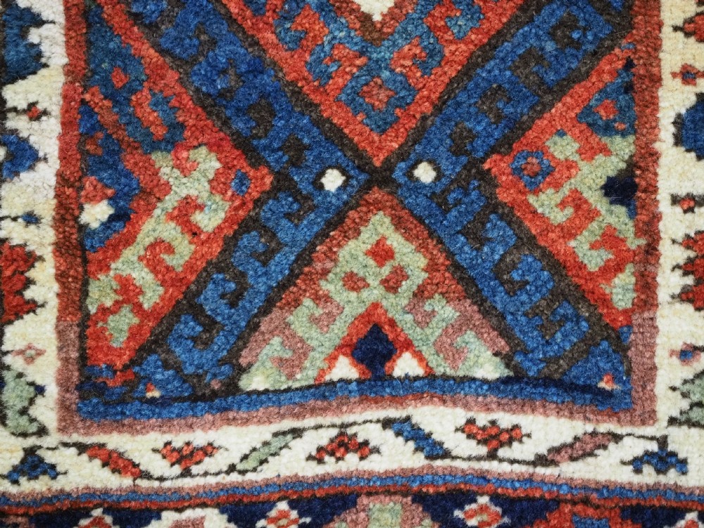 A hand-woven antique Kurdish Jaf bag featuring geometric diamond latch-hook motifs in red, blue, and cream wool with woven loops along the top edge. View VIII