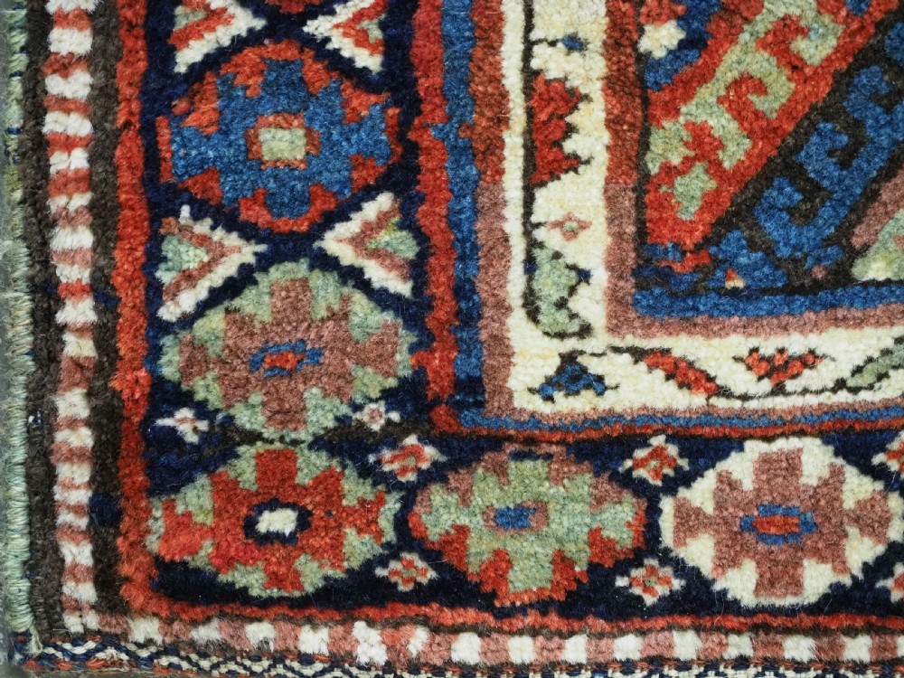 A hand-woven antique Kurdish Jaf bag featuring geometric diamond latch-hook motifs in red, blue, and cream wool with woven loops along the top edge. View IX