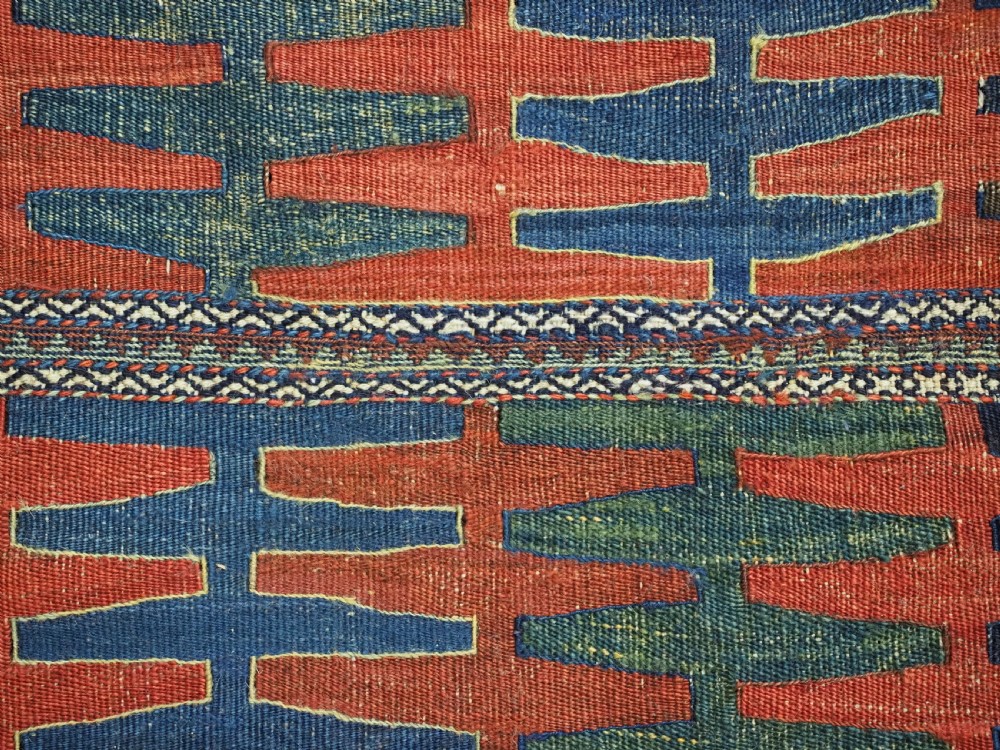 A hand-woven antique Kurdish Jaf bag featuring geometric diamond latch-hook motifs in red, blue, and cream wool with woven loops along the top edge. View XI