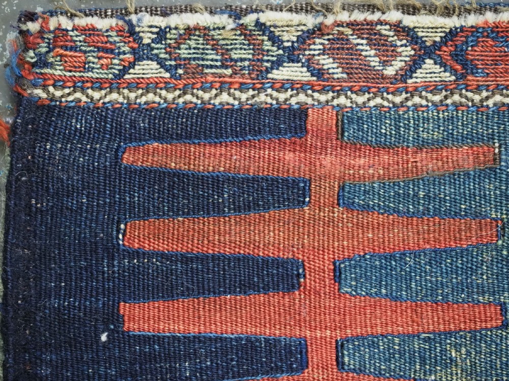 A hand-woven antique Kurdish Jaf bag featuring geometric diamond latch-hook motifs in red, blue, and cream wool with woven loops along the top edge. View XII