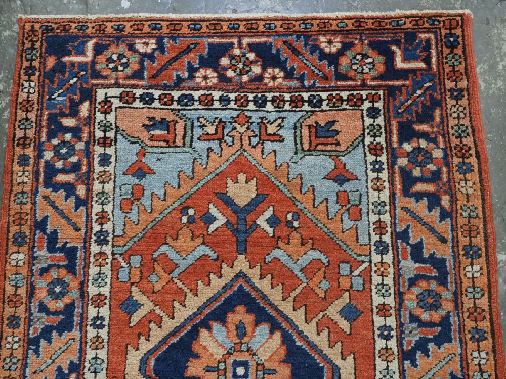 A small rectangular hand-knotted antique Persian Karaja rug featuring central diamond medallions on a terracotta field with blue geometric borders. View III