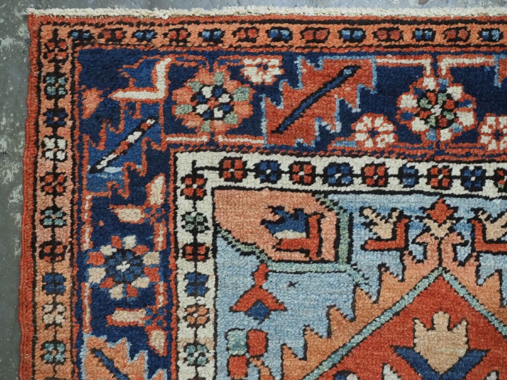 A small rectangular hand-knotted antique Persian Karaja rug featuring central diamond medallions on a terracotta field with blue geometric borders. View VI