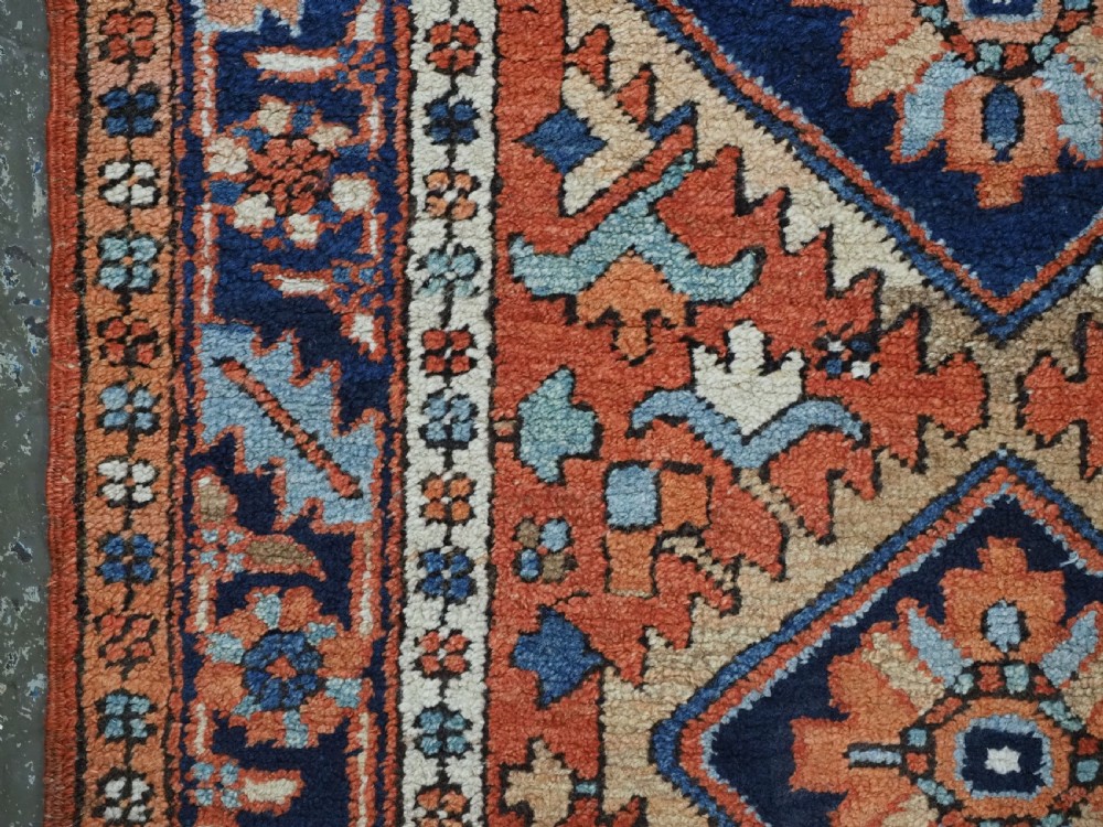 A small rectangular hand-knotted antique Persian Karaja rug featuring central diamond medallions on a terracotta field with blue geometric borders. View VII