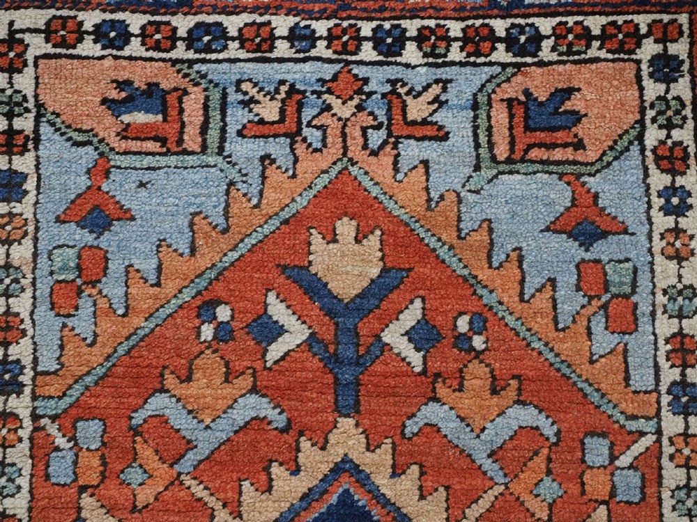 A small rectangular hand-knotted antique Persian Karaja rug featuring central diamond medallions on a terracotta field with blue geometric borders. View VIII