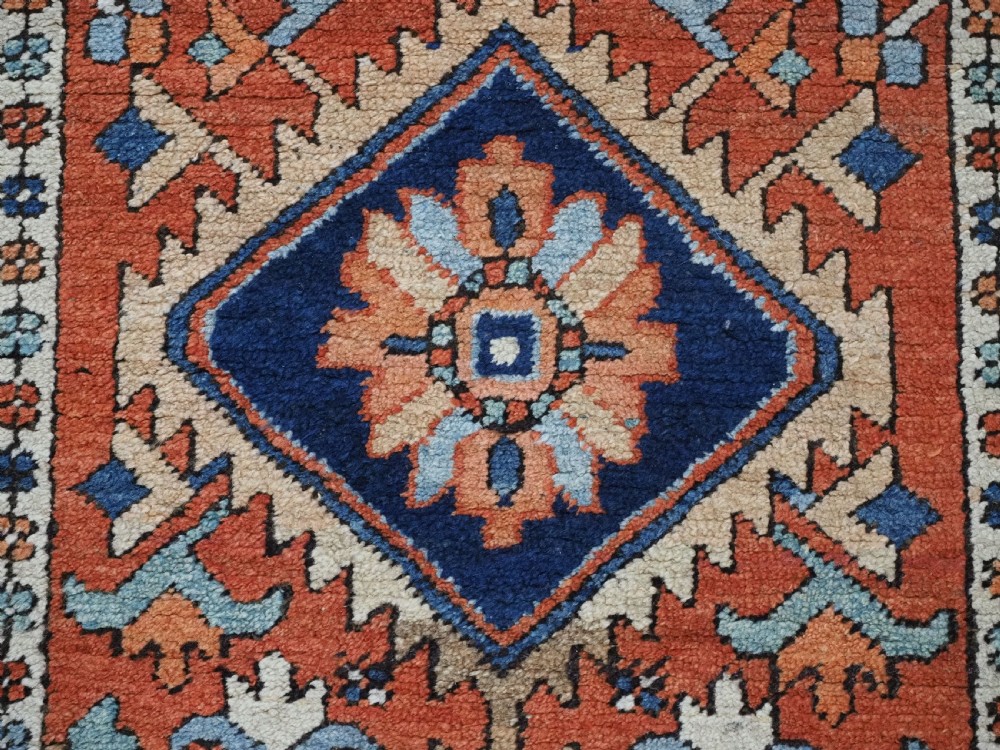 A small rectangular hand-knotted antique Persian Karaja rug featuring central diamond medallions on a terracotta field with blue geometric borders. View IX