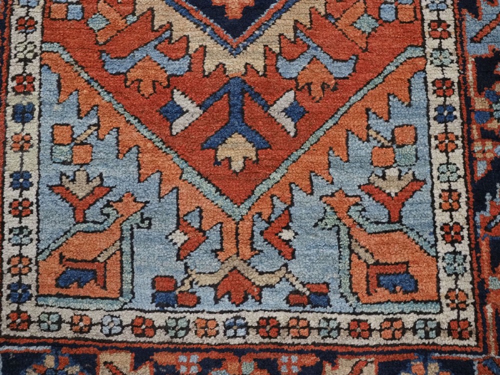 A small rectangular hand-knotted antique Persian Karaja rug featuring central diamond medallions on a terracotta field with blue geometric borders. View XI