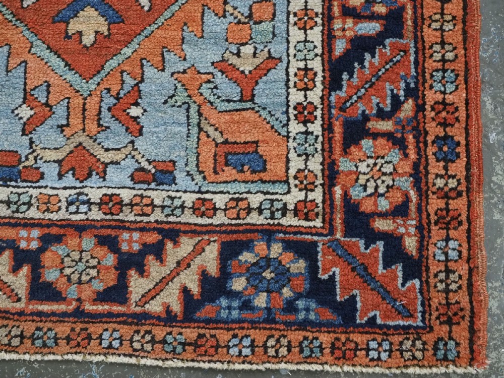 A small rectangular hand-knotted antique Persian Karaja rug featuring central diamond medallions on a terracotta field with blue geometric borders. View XII