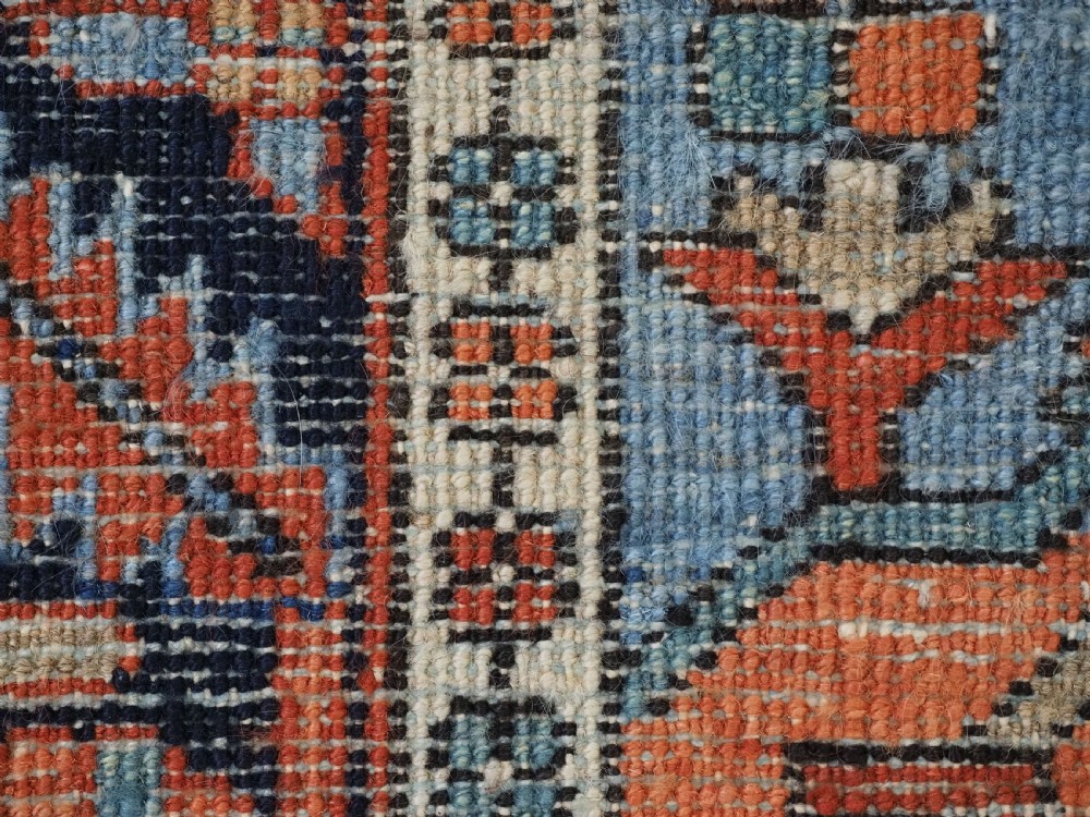 A small rectangular hand-knotted antique Persian Karaja rug featuring central diamond medallions on a terracotta field with blue geometric borders. View XIII
