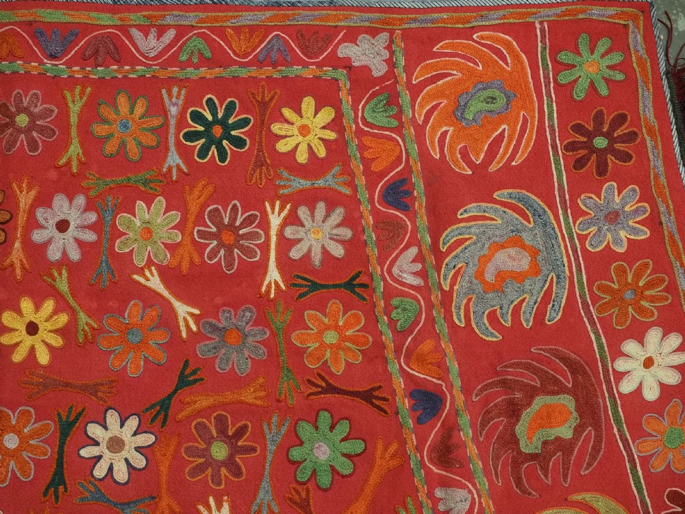 A trapezoidal Central Asian textile featuring dense multi-coloured floral, boteh, and horn embroidery on a red background with fringed edges. View VI