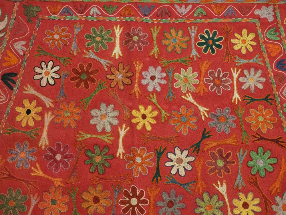 A trapezoidal Central Asian textile featuring dense multi-coloured floral, boteh, and horn embroidery on a red background with fringed edges. View VII
