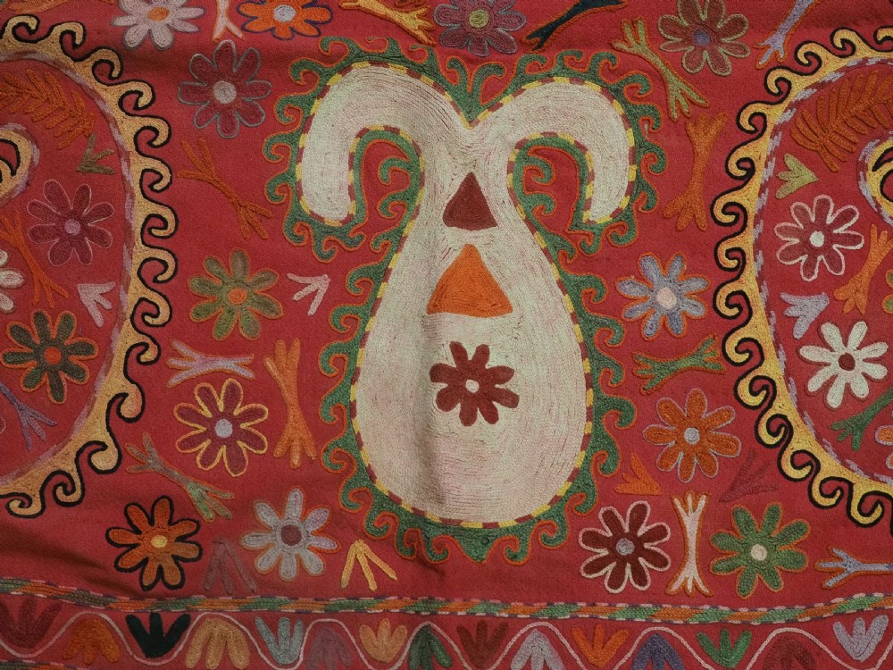 A trapezoidal Central Asian textile featuring dense multi-coloured floral, boteh, and horn embroidery on a red background with fringed edges. View VIII