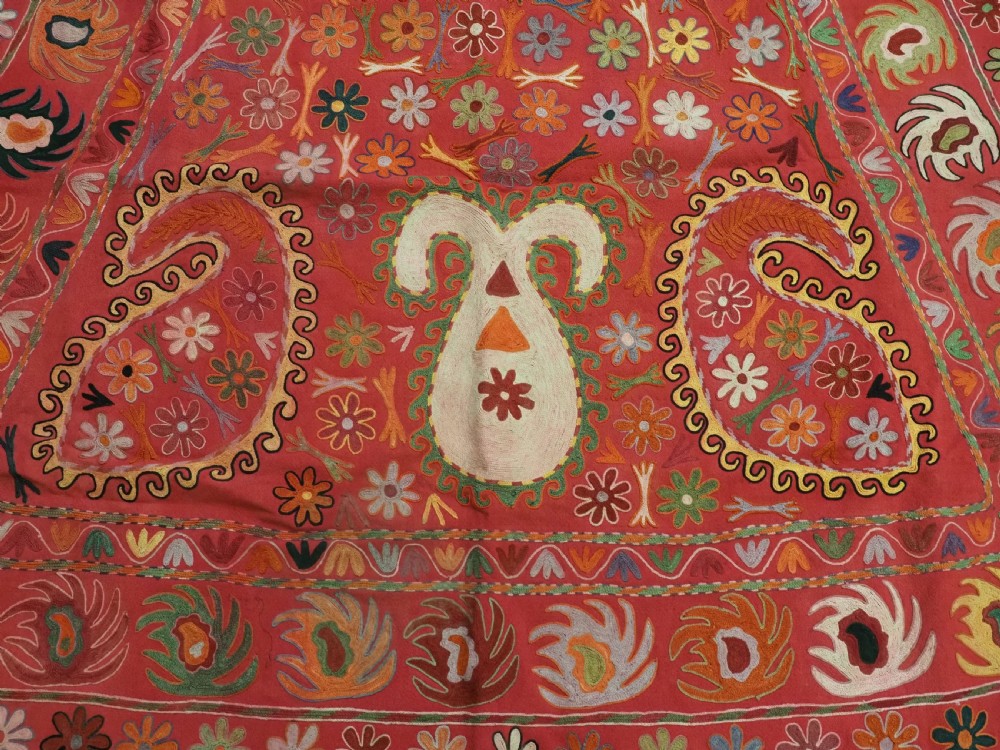 A trapezoidal Central Asian textile featuring dense multi-coloured floral, boteh, and horn embroidery on a red background with fringed edges. View IX