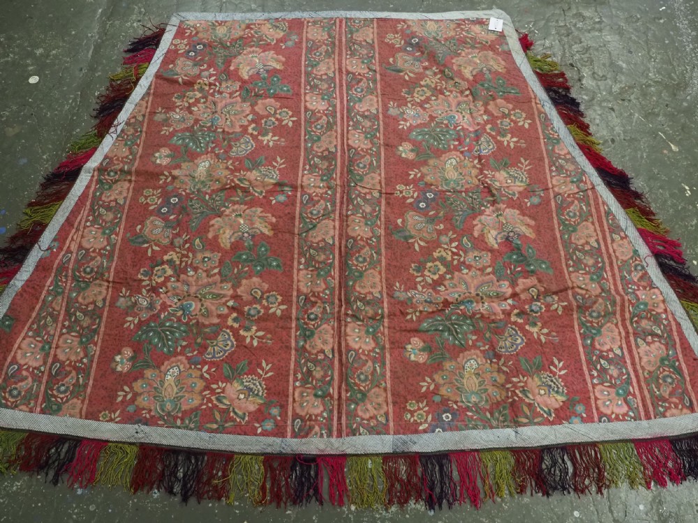 A trapezoidal Central Asian textile featuring dense multi-coloured floral, boteh, and horn embroidery on a red background with fringed edges. View XIV