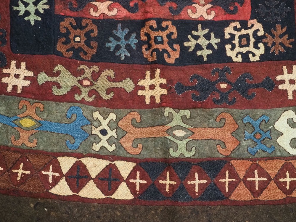 An antique Central Asian embroidered felt rug featuring a terracotta red centre with diamond medallions surrounded by multi-coloured geometric borders on dark brown felt. View XIV