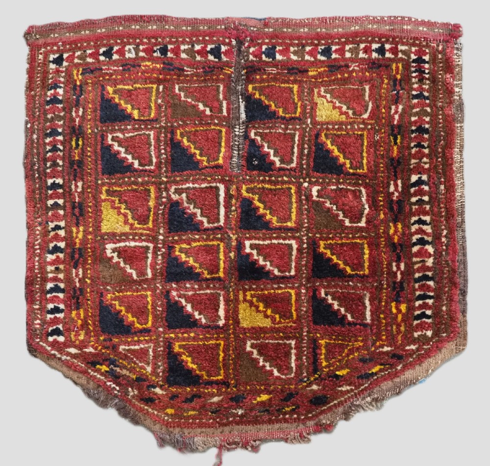 An antique Ersari Turkmen wool saddle cover featuring a grid layout of stepped geometric motifs in red, navy, yellow, and ivory.