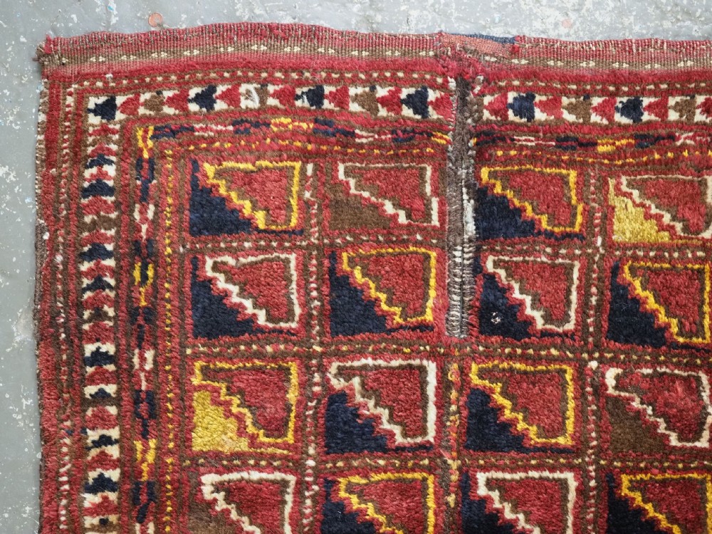 An antique Ersari Turkmen wool saddle cover featuring a grid layout of stepped geometric motifs in red, navy, yellow, and ivory. View II