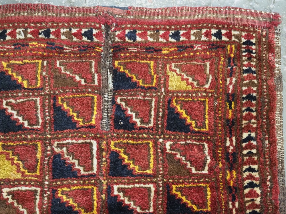 An antique Ersari Turkmen wool saddle cover featuring a grid layout of stepped geometric motifs in red, navy, yellow, and ivory. View IV