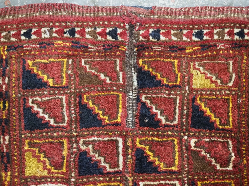 An antique Ersari Turkmen wool saddle cover featuring a grid layout of stepped geometric motifs in red, navy, yellow, and ivory. View VI