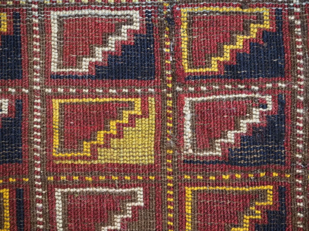 An antique Ersari Turkmen wool saddle cover featuring a grid layout of stepped geometric motifs in red, navy, yellow, and ivory. View IX