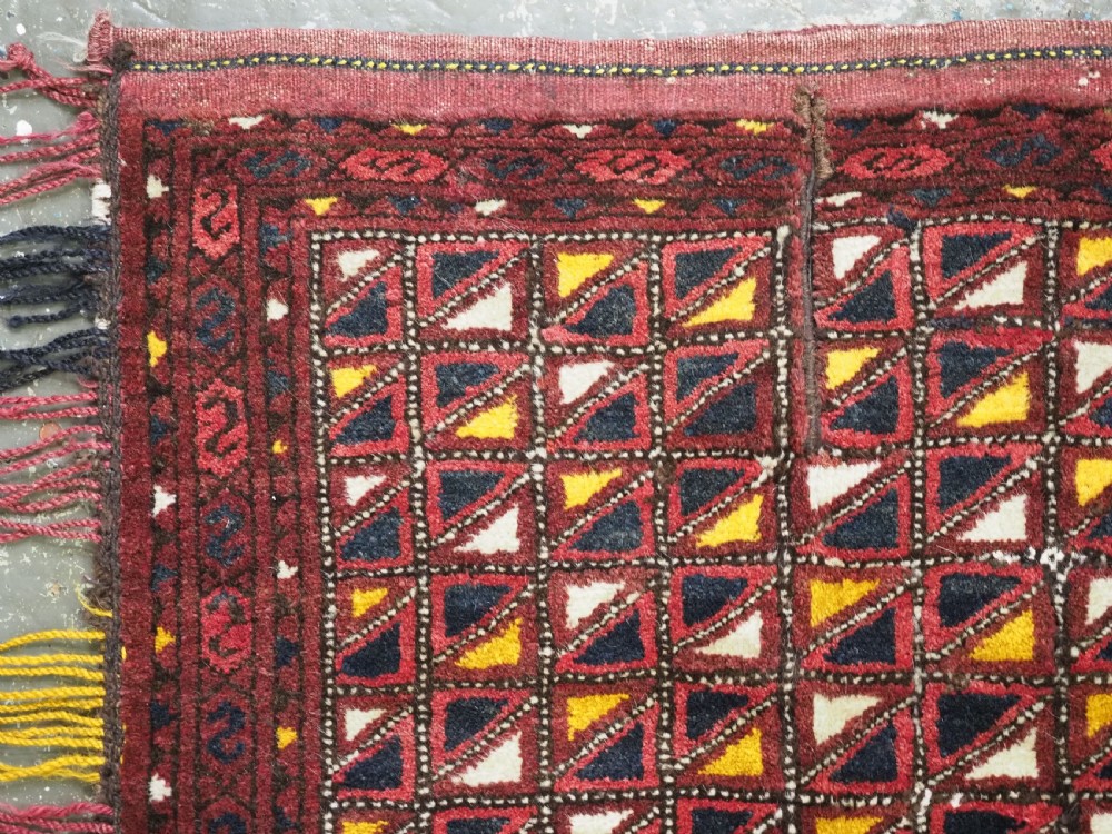 An antique Ersari Turkmen saddle cover rug with a grid pattern of triangular motifs in red, navy, yellow, and white, trimmed with multi-coloured yarn tassels. View II