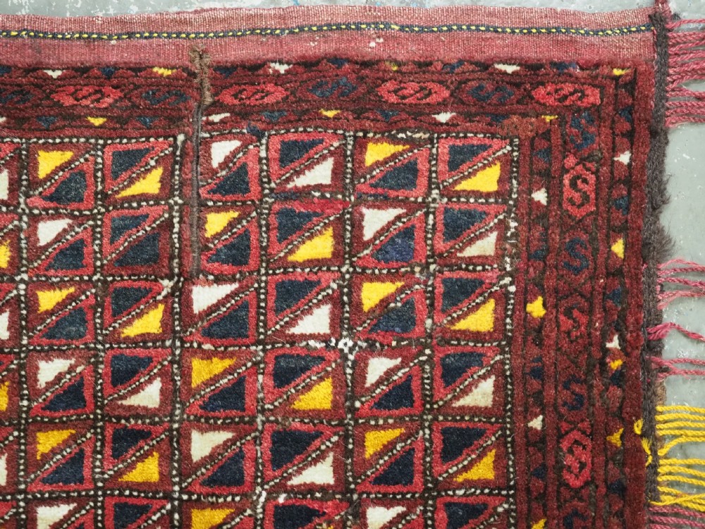 An antique Ersari Turkmen saddle cover rug with a grid pattern of triangular motifs in red, navy, yellow, and white, trimmed with multi-coloured yarn tassels. View III