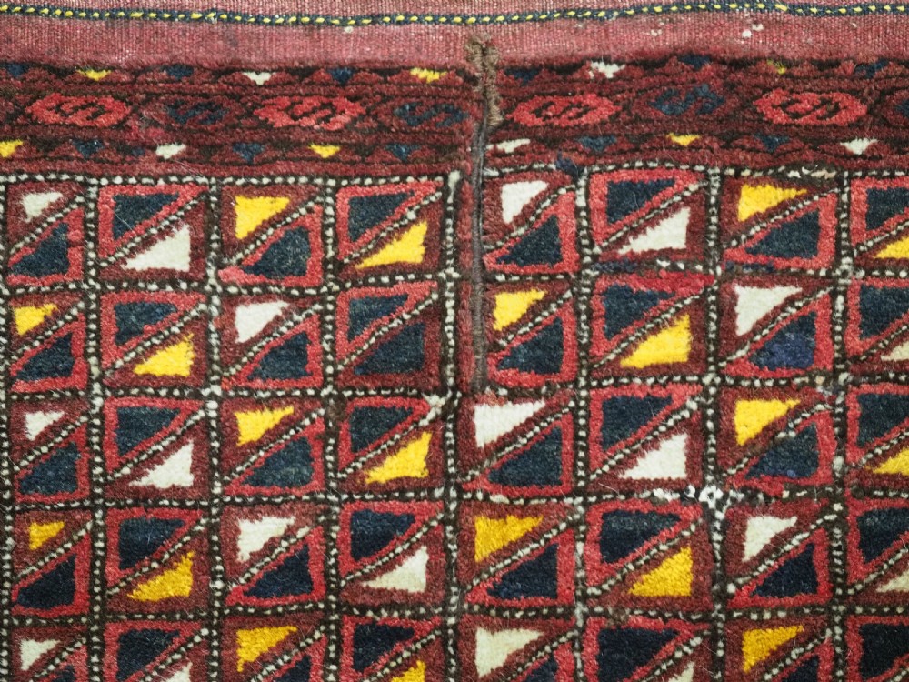 An antique Ersari Turkmen saddle cover rug with a grid pattern of triangular motifs in red, navy, yellow, and white, trimmed with multi-coloured yarn tassels. View VI