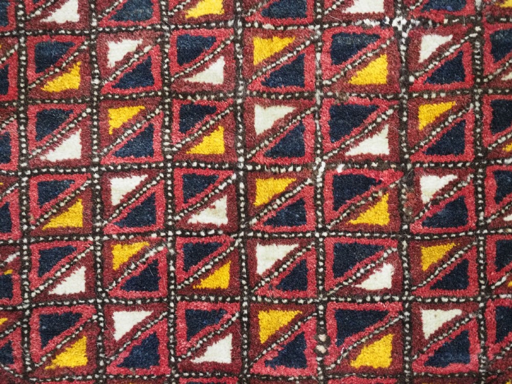An antique Ersari Turkmen saddle cover rug with a grid pattern of triangular motifs in red, navy, yellow, and white, trimmed with multi-coloured yarn tassels. View VII