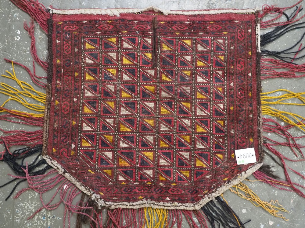 An antique Ersari Turkmen saddle cover rug with a grid pattern of triangular motifs in red, navy, yellow, and white, trimmed with multi-coloured yarn tassels. View VIII
