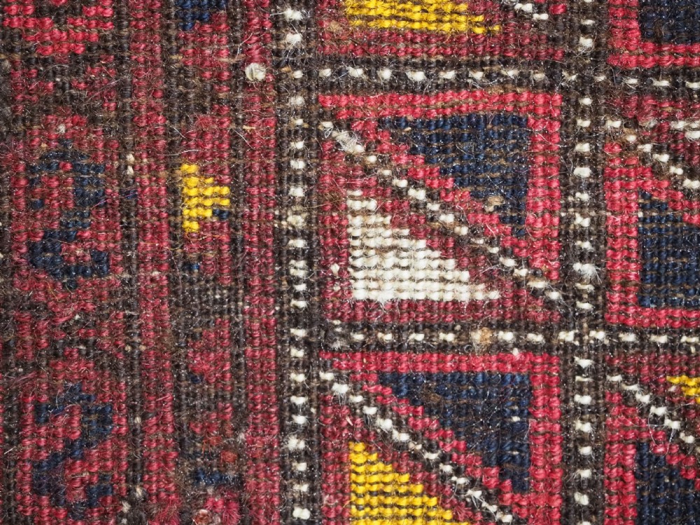 An antique Ersari Turkmen saddle cover rug with a grid pattern of triangular motifs in red, navy, yellow, and white, trimmed with multi-coloured yarn tassels. View IX