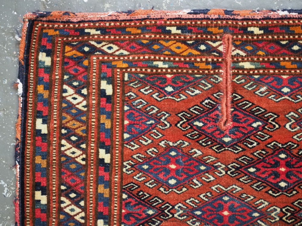 A handwoven Yomut Turkmen wool saddle cover featuring geometric diamond motifs in terracotta red, dark blue, and ivory with a central saddle horn slit. View II