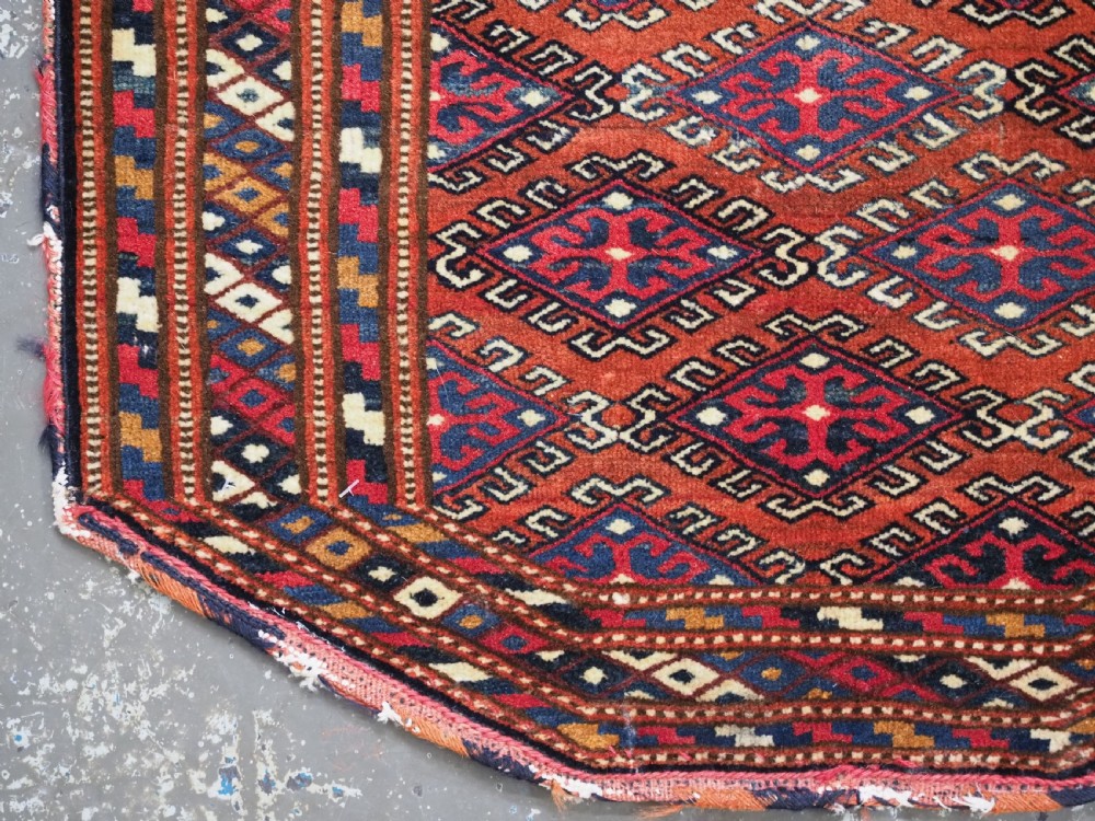 A handwoven Yomut Turkmen wool saddle cover featuring geometric diamond motifs in terracotta red, dark blue, and ivory with a central saddle horn slit. View IV