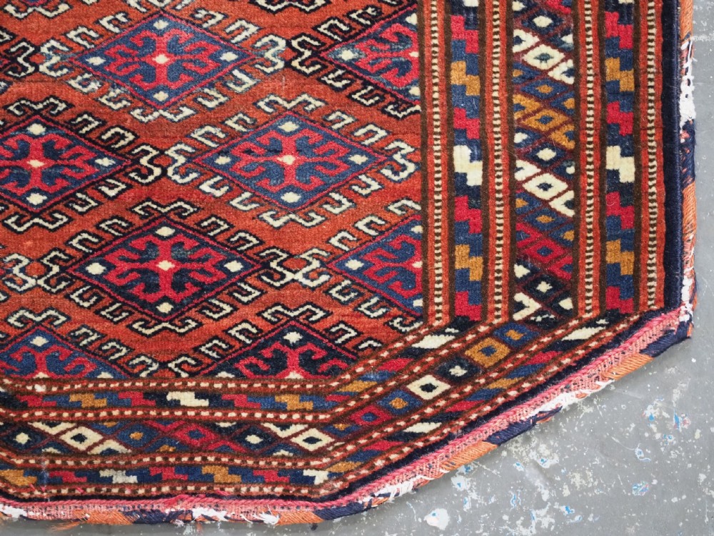 A handwoven Yomut Turkmen wool saddle cover featuring geometric diamond motifs in terracotta red, dark blue, and ivory with a central saddle horn slit. View V