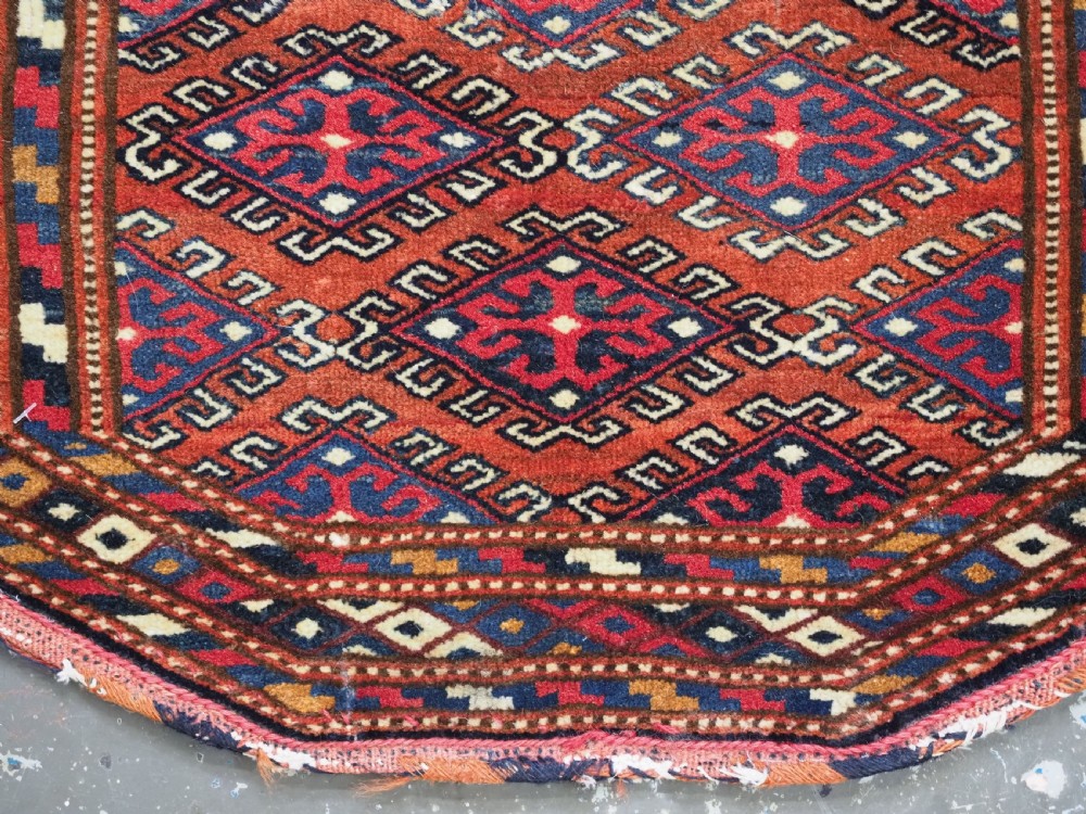 A handwoven Yomut Turkmen wool saddle cover featuring geometric diamond motifs in terracotta red, dark blue, and ivory with a central saddle horn slit. View VII
