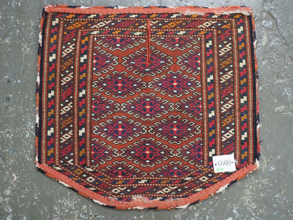 A handwoven Yomut Turkmen wool saddle cover featuring geometric diamond motifs in terracotta red, dark blue, and ivory with a central saddle horn slit. View VIII
