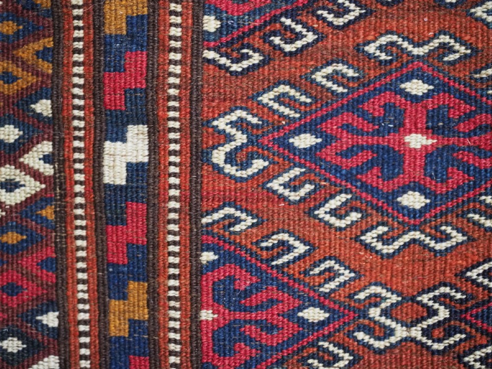 A handwoven Yomut Turkmen wool saddle cover featuring geometric diamond motifs in terracotta red, dark blue, and ivory with a central saddle horn slit. View IX