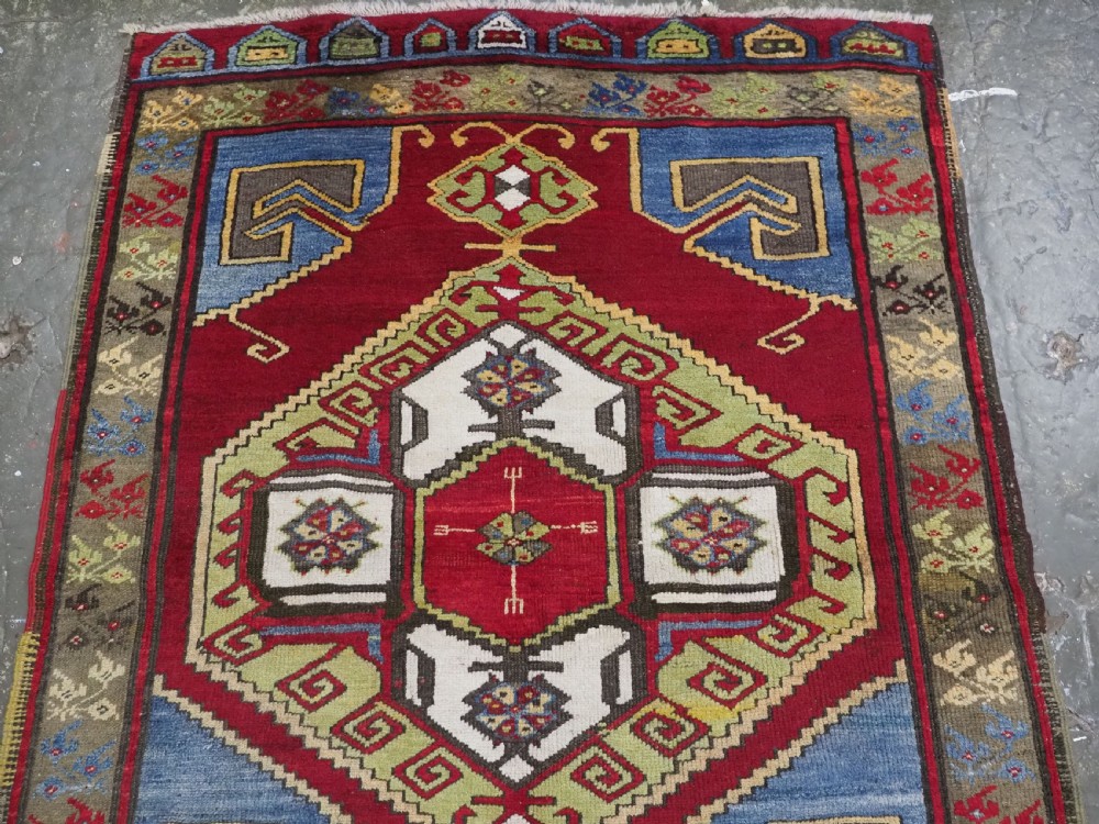An antique Turkish long wool rug featuring three primary geometric medallions on a vibrant red field with blue and patterned border panels. View III