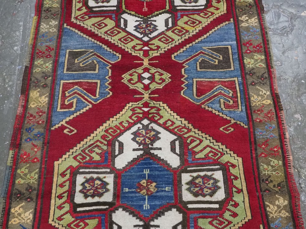 An antique Turkish long wool rug featuring three primary geometric medallions on a vibrant red field with blue and patterned border panels. View IV
