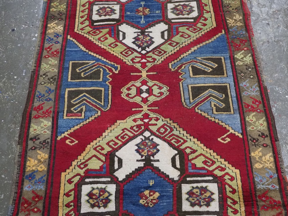 An antique Turkish long wool rug featuring three primary geometric medallions on a vibrant red field with blue and patterned border panels. View V