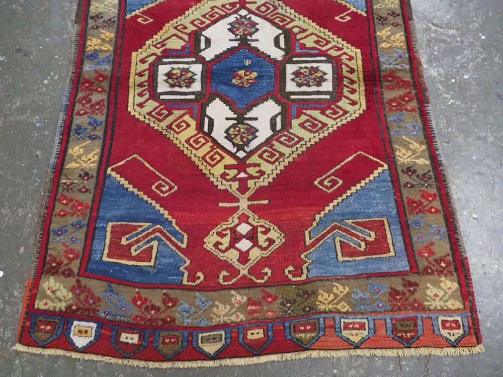 An antique Turkish long wool rug featuring three primary geometric medallions on a vibrant red field with blue and patterned border panels. View VI