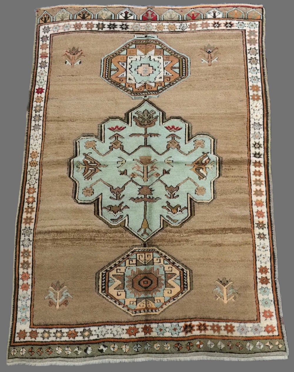An antique hand-knotted Turkish Konya Karapinar rug featuring a camel wool field and geometric medallions in turquoise and terracotta.