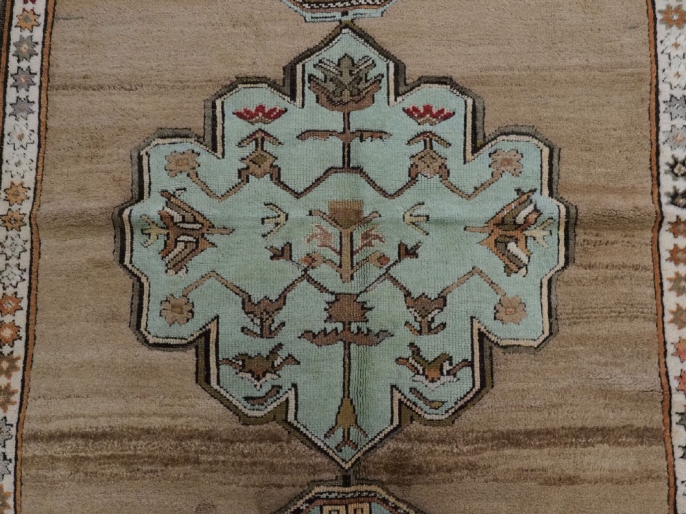 An antique hand-knotted Turkish Konya Karapinar rug featuring a camel wool field and geometric medallions in turquoise and terracotta. View X
