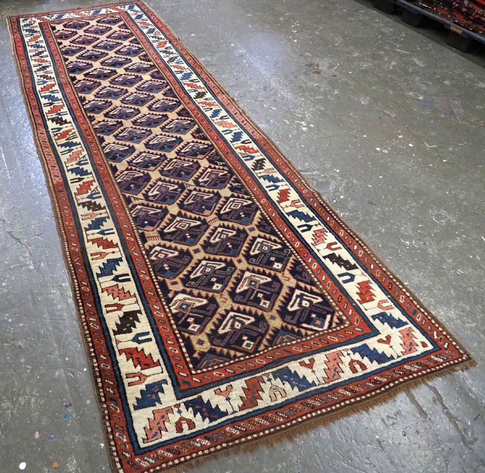 An antique Caucasian wool rug runner featuring a central geometric lattice pattern in navy blue and cream within multiple decorative borders. View II