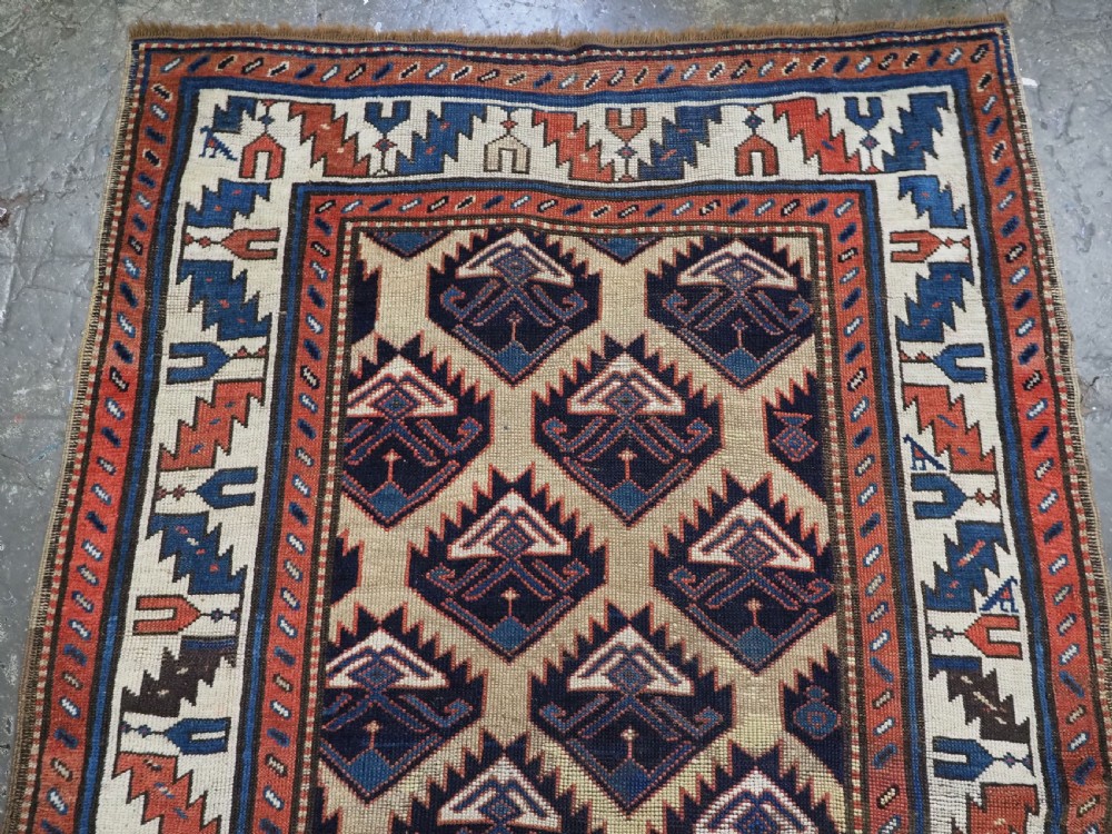 An antique Caucasian wool rug runner featuring a central geometric lattice pattern in navy blue and cream within multiple decorative borders. View III