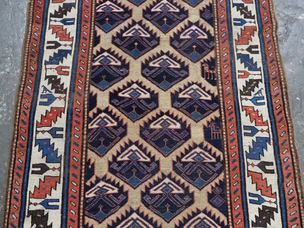An antique Caucasian wool rug runner featuring a central geometric lattice pattern in navy blue and cream within multiple decorative borders. View IV
